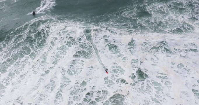 Aerial drone shot of big wave surfer surfing a big wave on a day with giant waves in Nazare, Portugal, Europe. Nazaré, big wave surfing town with biggest waves in the world. Shot in ProRes 422 HQ