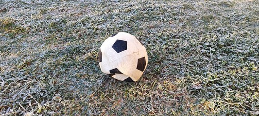 A deflated soccer ball on frosty green grass. Old forgotten football on a cold winter morning. Outdoor sports concept