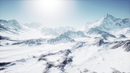 Majestic mountains rise sharply against the backdrop of a clear blue sky. Bright sunlight illuminates the snow covered peaks, creating a serene and breathtaking winter scene.