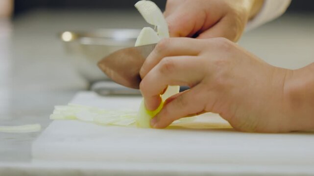 Close-up of a chef's hands cutting a peeled green apple into thin slices on a white chopping board and carefully placing them in an aluminum mold on a kitchen counter.