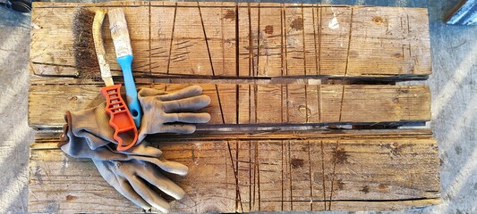Work tools including gloves and brushes on a rustic wooden workbench. DIY and home improvement...