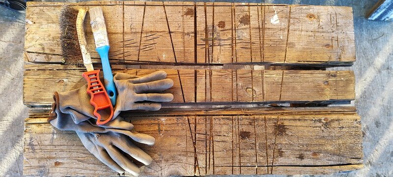 Work tools including gloves and brushes on a rustic wooden workbench. DIY and home improvement concept. Top view flat lay with copy space