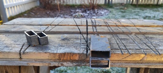 Cut steel tubing on a rustic wooden workbench. DIY metalworking and construction project. Outdoor workshop scene on a cold morning