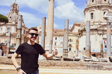 Fototapeta premium Boy enjoying view on the Roman Forum, ruins at the center of Rome on a sunset. Concept of traveling famous landmarks in Italy. Caucasian Boy tourist making a photo with a phone 