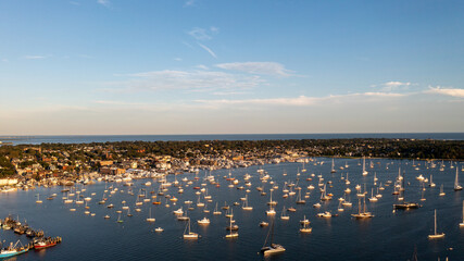 Aerial view of boats bobbing gently on the serene, deep blue waters of the harbor, framed by the quaint coastal town and distant shoreline, Newport, Rhode Island, United States.