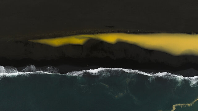 Aerial view of a stark contrast where the golden river meets the dark sand beach and the turquoise ocean, Isafjordur, Iceland.
