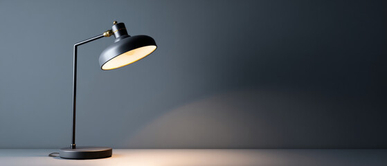 Modern black desk lamp illuminating surface against dark gray background with soft focused light and minimalist design
