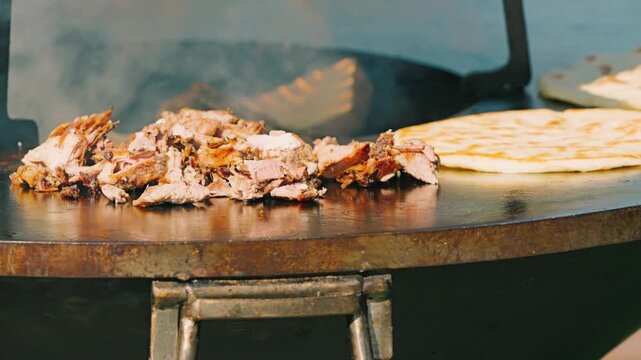 A close-up of a gloved hand laying out pieces of masa on a hot grill. Rising smoke adds a delicious ambiance to the cooking process. Flatbreads are frying nearby