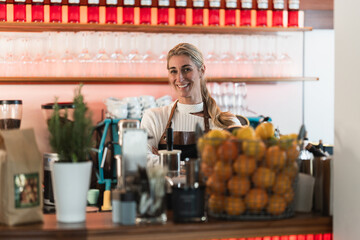 A cheerful waitress behind the counter poses with a warm smile showing friendly cafe service in a bright coffee shop