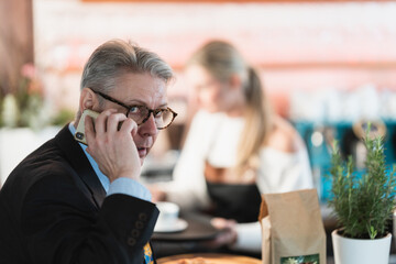 A middle aged businessman sits at the bar speaking on his smartphone creating a modern professional portrait in a casual setting