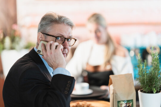 A professional middle aged businessman at the bar speaks on his smartphone capturing a modern corporate lifestyle portrait