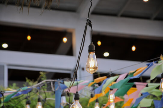 String lights featuring vintage Edison bulbs and colorful bunting decorations hanging outdoors for a festive event or party - Powered by Adobe