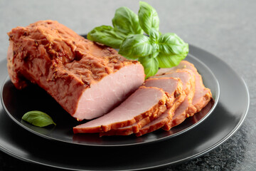 Smoked ham with basil on a black plate.