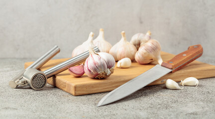 Garlic, knife, and garlic press on a cutting board.