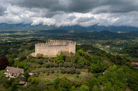 Aerial view of Rocca di Asolo standing proudly atop a lush green hill under a dramatic sky, the ancient stone walls contrasting with the vibrant foliage, Asolo, Veneto, Italy.