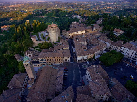 Aerial view of ancient buildings and the Rocca Fortress nestled among the green hillsides under a golden sunset light, Asolo, Veneto, Italy.