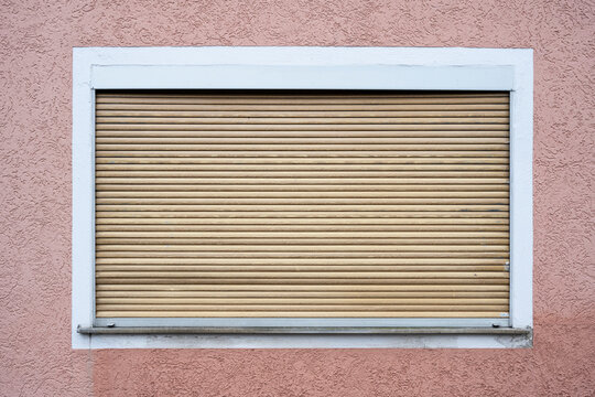 Tall window on a wall, wooden shutter rolled up and closed, wall pink painted