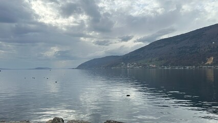 Wide panoramic view of Lake Biel with gentle ripples, cloudy dramatic sky and forested hills stretching along the shoreline.
