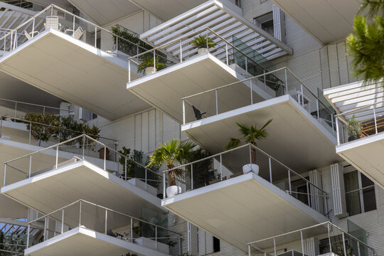 View of staggered balconies decorated with lush greenery protruding from a modern white building under a bright sky, forming a striking geometric pattern, Montpellier, Occitanie, France.