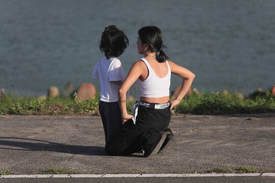 Taipei, Taiwan - November 15th 2025: Rear view of mother and child kneeling and looking at river view in park.