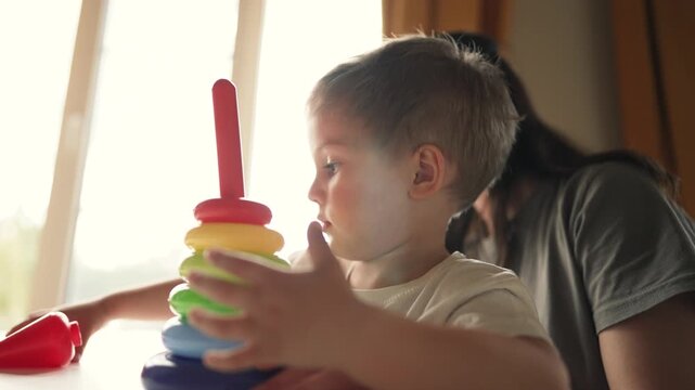 Toddler stacks colorful toy ring while parent supports from behind child explores learning through play with family in indoor setting hands arranging ring to study color shape and fine motor skill