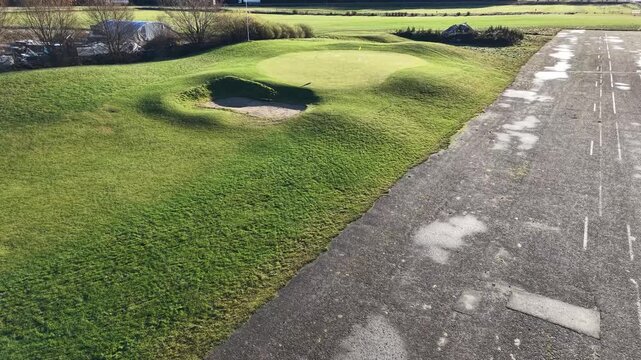 Valmiera, Latvia - November 18, 2025: Aerial view of golf course green with sand trap and pathway, camera pans across lush landscape