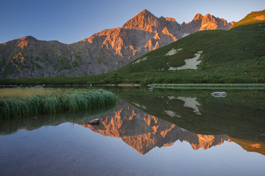 View of the majestic, sun-kissed mountain peaks reflecting in the calm waters of Biele pleso tarn, creating a serene landscape, Biele pleso, Presovsky kraj, Slovakia.