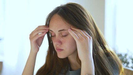 Young woman massaging temple from headache while showing stress and pain expression migraine concern tension fatigue posture indoor soft light closeup emotional face conveying discomfort and tiredness - Powered by Adobe
