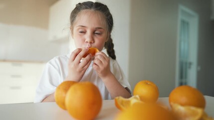 Girl peeling orange and tasting slice child sits at kitchen table surrounded by orange fruit exploring flavor and texture of peeled segment for healthy snack eating and citrus aroma and juice and peel - Powered by Adobe