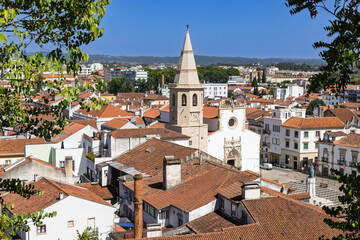 Elevated view over the terracotta rooftops of Tomar, Portugal, centered on the striking bell tower...