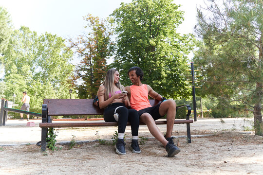 Athletes relaxing on bench and using smartphone after training in park