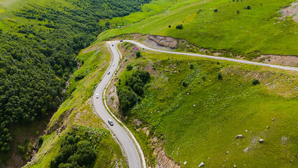 The car is driving along a winding serpentine road in the Caucasus Mountains to the Dzhila Valley.