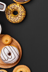 Stack of glazed colorful assorted donuts with sprinkles on black background.