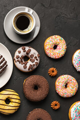Stack of glazed colorful assorted donuts with sprinkles on black background.