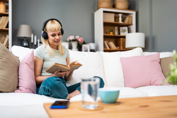 Young woman reading a book with headphones on, mixing quiet study and background music; turning...