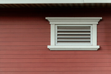 White wooden ventilation louver window on red timber wall siding offering minimalist architectural detail.