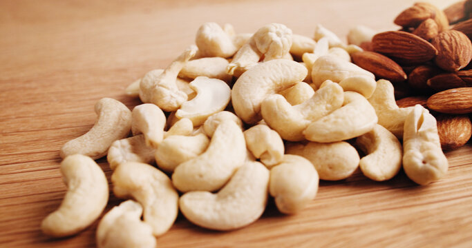 Kitchen, nuts and cashews on table for diet, vegan snack and healthy food for nutrition. Empty, background and harvest of roasted almonds on wooden counter for organic fats, vitamins and protein - Powered by Adobe