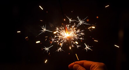 Sparkler burning brightly in the dark, creating a dazzling display of light and sparks, held by a hand