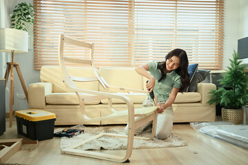 Young woman assembling new furniture at home with screwdriver, DIY home improvement