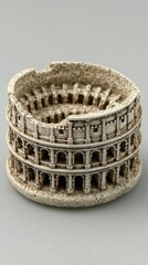 Detailed miniature replica of the Colosseum structure showing intricate architectural details and a textured surface presented on a plain grey studio backdrop.