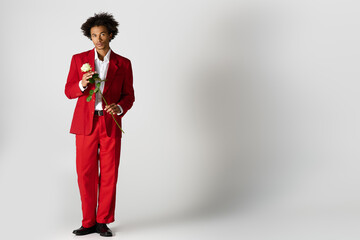Elegant young man in striking red suit holding a rose for a romantic moment