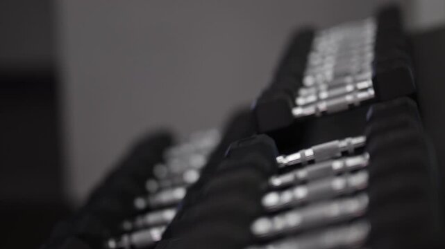 A young woman in a modern gym taking dumbbells from an organized rack before starting her workout. Stylish fitness environment with clean equipment, showcasing strength training and active lifestyle.