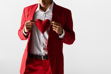 Young man in elegant red attire holds heart symbol with charm and confidence in a stylish setting