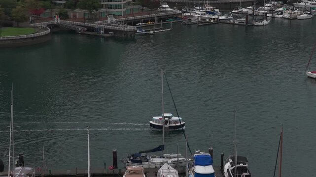Telephoto aerial tracking shot of the False Creek Ferry arriving at Granville Island on a rainy morning in Vancouver, British Columbia, Canada. 4K