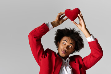 Young handsome man in elegant red attire expresses joy while holding a heart shaped pillow