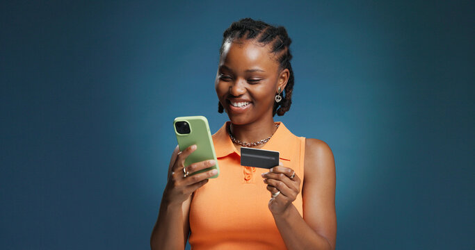 Happy, black woman and credit card with phone in studio for online shopping on a blue background. Female person, shopper or user with mobile smartphone or debit for banking app or ecommerce on space