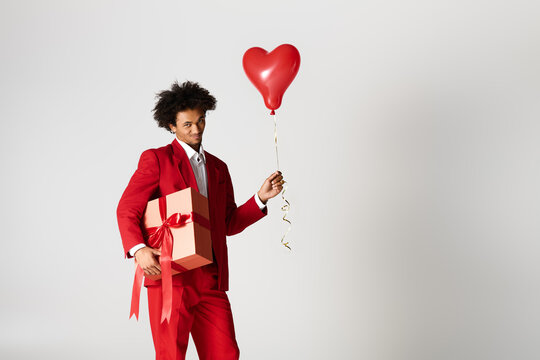 Young man in elegant red suit holds gift and heart balloon in a joyful celebration