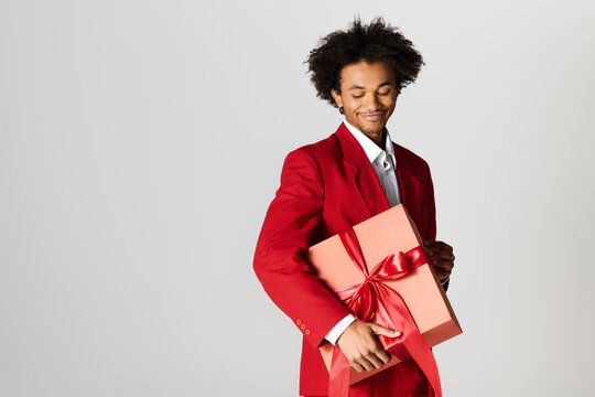 Handsome young man in elegant red suit holding a beautifully wrapped gift with a joyful smile