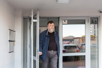 Bearded senior Caucasian man coming out of an apartment building