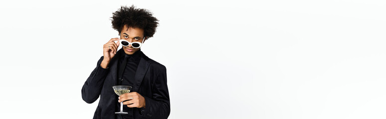 Young man in elegant attire enjoys a stylish drink while striking a confident pose